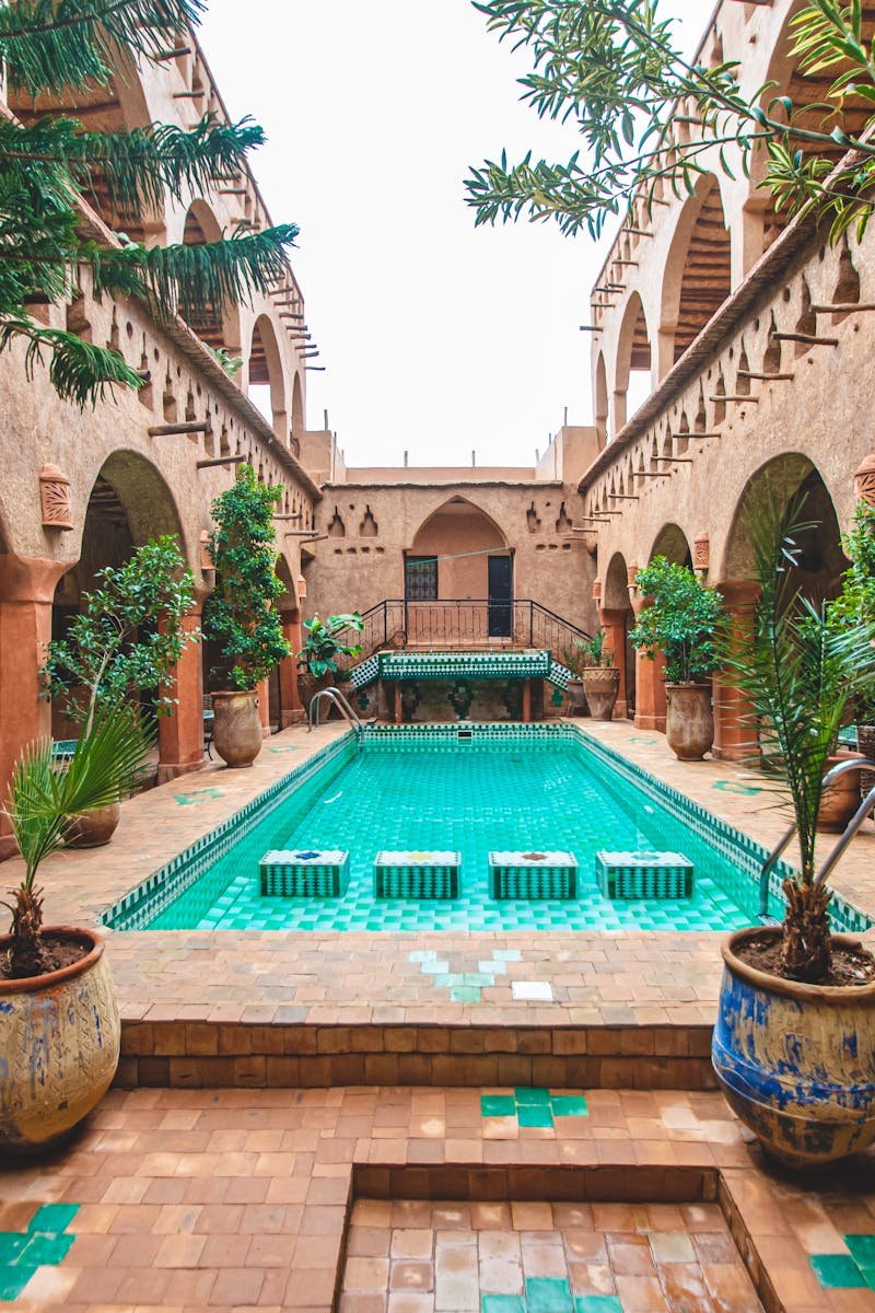 Charming pool courtyard of a traditional riad in Ouarzazate, Morocco, with lush plants and intricate architecture.