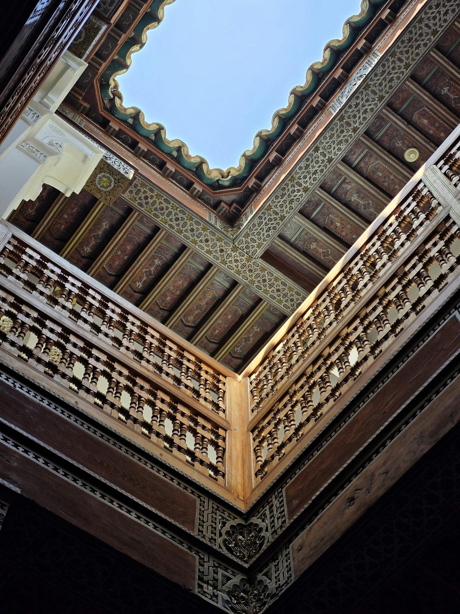 View of a beautifully intricate Moroccan courtyard with ornate wooden railings and open sky.